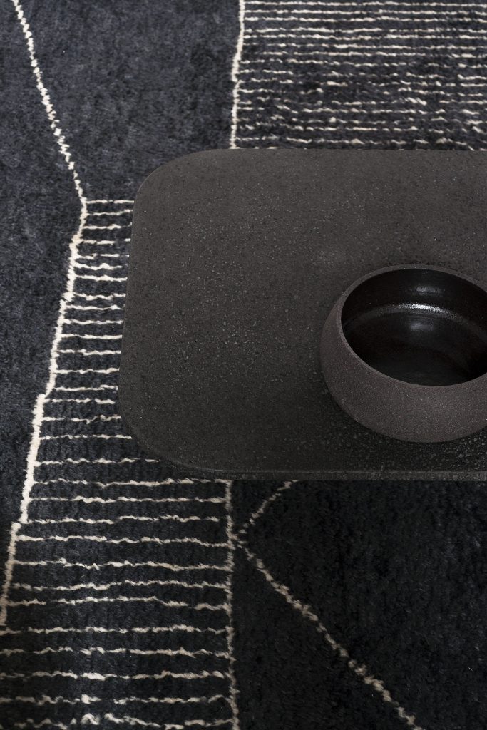 Berbère Dark Grey + Natural | Pattern A. Rug decorated with a woolen stitching with a table as decor.