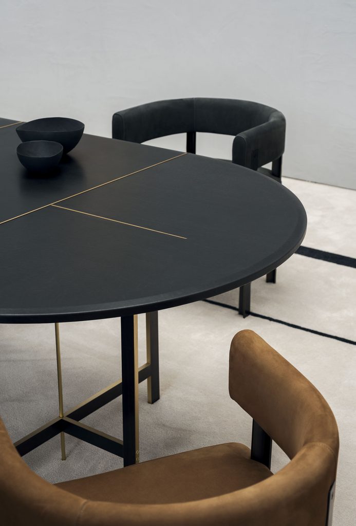 A Placè Dining Table. Base in brass with bronzing oxidation on the flat part and satin finish on the thickness, with wax finish. Leg connection plate in matte black metal. MDF top with reinforcing black leather-covered aluminium sheets. Decorative inserts in satin-finished brass with wax finish.