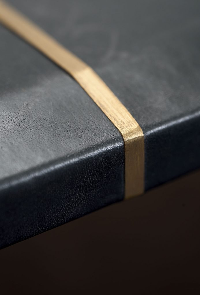 A Placè Dining Table. Base in brass with bronzing oxidation on the flat part and satin finish on the thickness, with wax finish. Leg connection plate in matte black metal. MDF top with reinforcing black leather-covered aluminium sheets. Decorative inserts in satin-finished brass with wax finish.