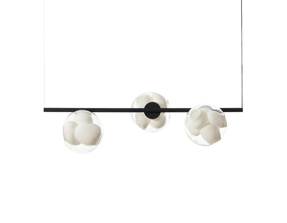 Boc Stem Suspended Ceiling Light showcases three white ceramic cluster spheres held in clear glass globes, aligned along a matte black horizontal rod. The composition floats against a crisp white background, emphasizing its minimal elegance.
