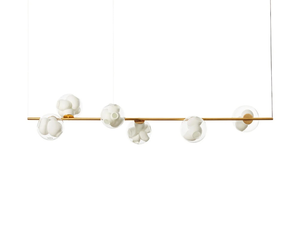 Boc Stem Suspended Ceiling Light extends across a golden rod with five evenly spaced glass spheres. Each sphere encloses white ceramic clusters, blending structure and softness with a modern, sculptural aesthetic.