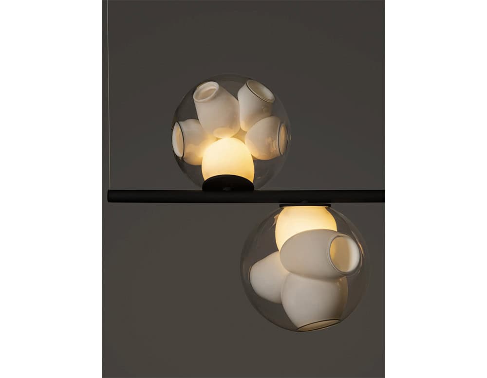 Boc Stem Suspended Ceiling Light features clusters of white ceramic pieces suspended within glass orbs, casting a warm, ambient glow that blends sculptural complexity with a minimalist form.