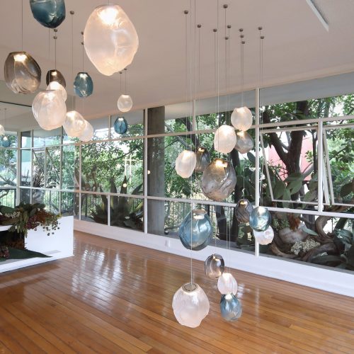 A Seventy Three V lamp in white, black and blue blown glass in fabric shape, braided metal coaxial cable, electrical components, brushed nickel in a living room.