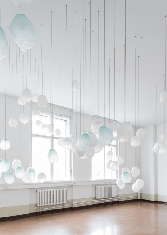 A Seventy Three V lamp in white and blue blown glass in fabric shape, braided metal coaxial cable, electrical components, brushed nickel in a white and a brown room.
