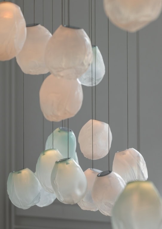 A Seventy Three V lamp in white and blue blown glass in fabric shape, braided metal coaxial cable, electrical components, brushed nickel in a grey background.