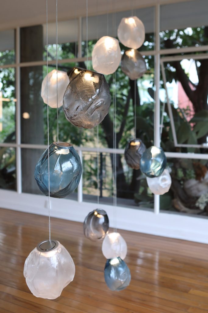 A Seventy Three V lamp in white, black and blue blown glass in fabric shape, braided metal coaxial cable, electrical components, brushed nickel in a living room.