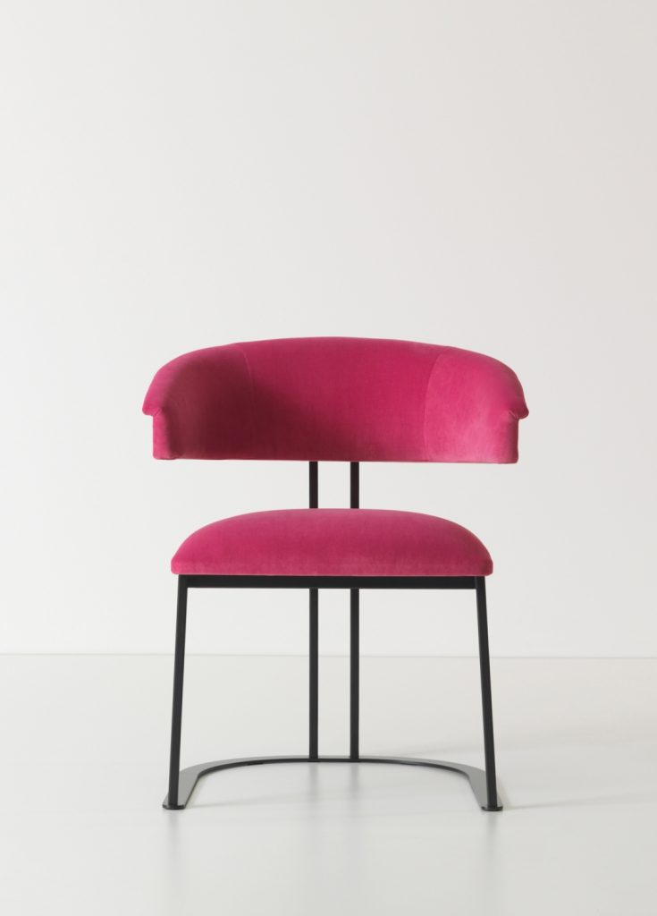 curved armchair made of pink leather and an iron and brass base on a white background