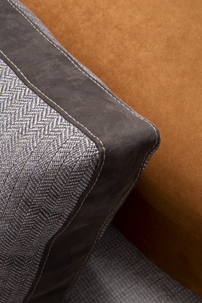 Closeup of Caprera Sofa: Large gray cushioned sofa with wooden frame and black legs.