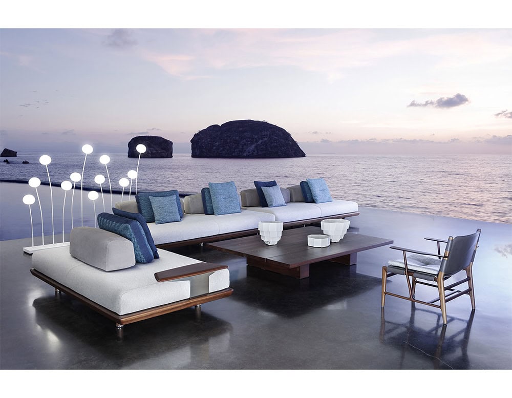 A luxurious outdoor lounge at sunset featuring the Joint Rectangular Coffee Table surrounded by modern seating ambient lighting and an ocean view