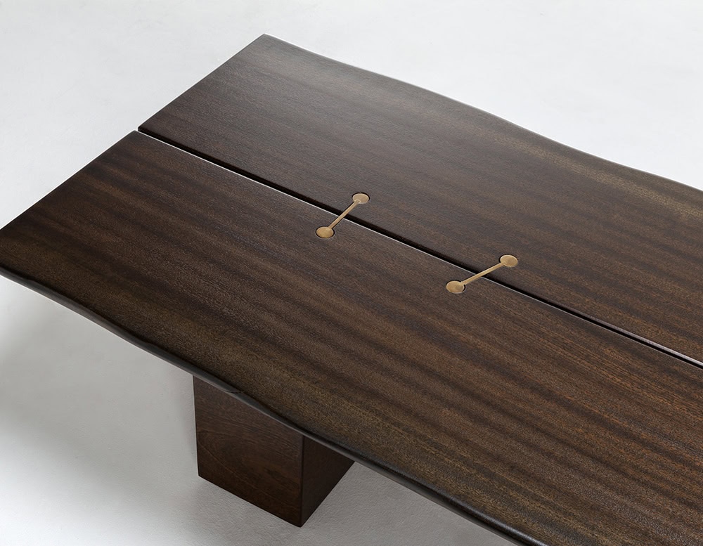 A 10th Joint Wood Coffee Table with a dark wood tabletop and a unique joinery detail featuring two brass fasteners is shown at an angle against a light background