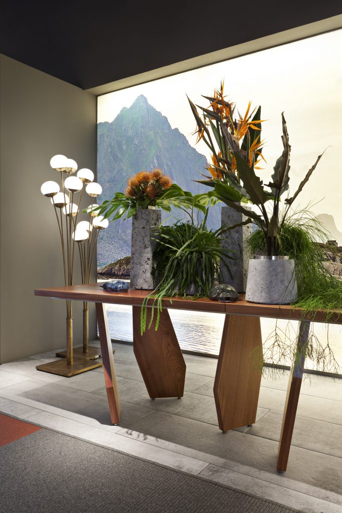 10th Joint Dinner Table: Long rectangular top in brown wood materic slabs connected by burnished brass joints and two polygonal legs in a dining room.
