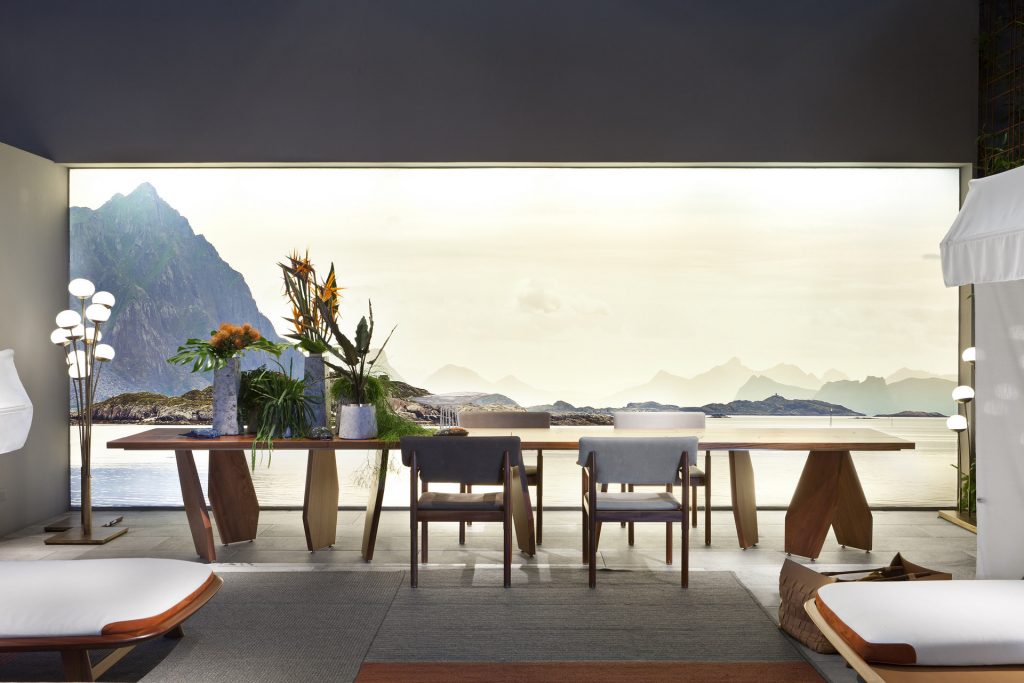 10th Joint Dinner Table: Long rectangular top in brown wood materic slabs connected by burnished brass joints and two polygonal legs in a dining room.