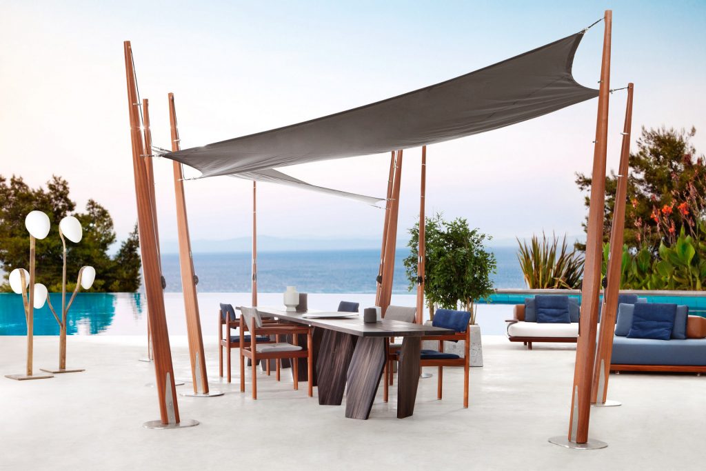 10th Joint Dinner Table: Long rectangular top in brown wood materic slabs connected by burnished brass joints and two polygonal legs on a terrace.