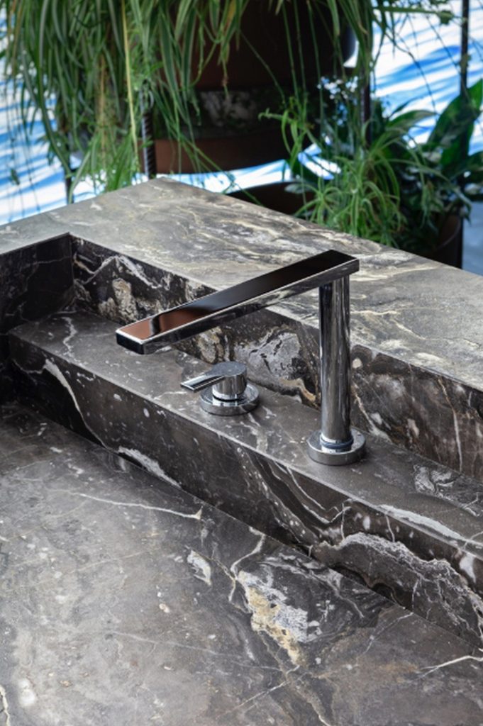 10th Kitchen: Modern kitchen setup made of gray stone, a central island and three brass cylindrical legs in a kitchen.