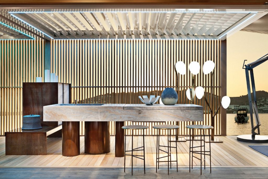 10th Kitchen: Modern kitchen setup made of gray stone, a central island and three brass cylindrical legs in a kitchen.