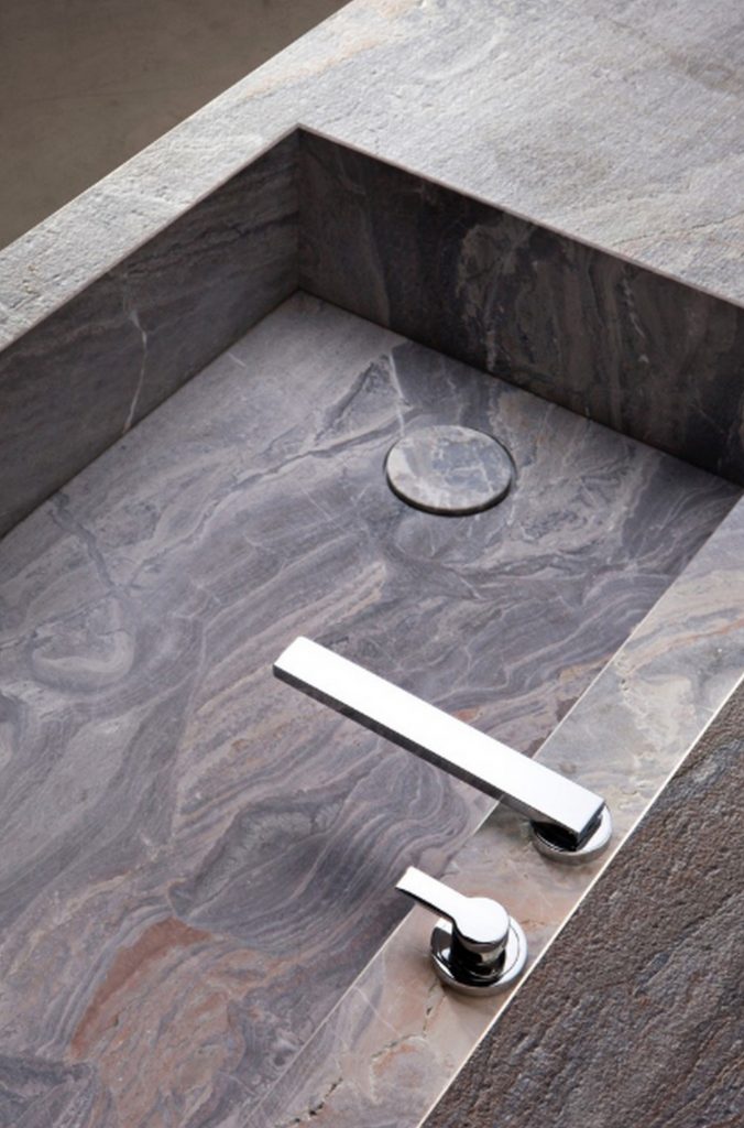 10th Kitchen: Modern kitchen setup made of gray stone, a central island and three brass cylindrical legs in a kitchen.