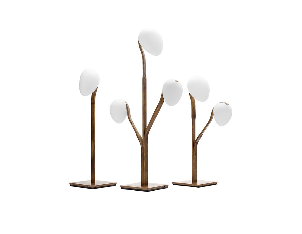 A studio shot of the 10th Tree Light Outdoor Floor Light collection showcasing three variations with elegantly curved wooden frames and smooth white diffusers
