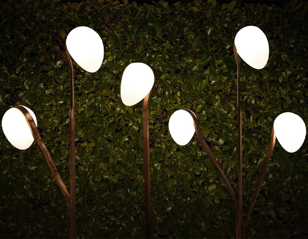 Several 10th Tree Light Outdoor Floor Lights with white, orb-shaped diffusers on slender stems are shown against a dark, blurred background