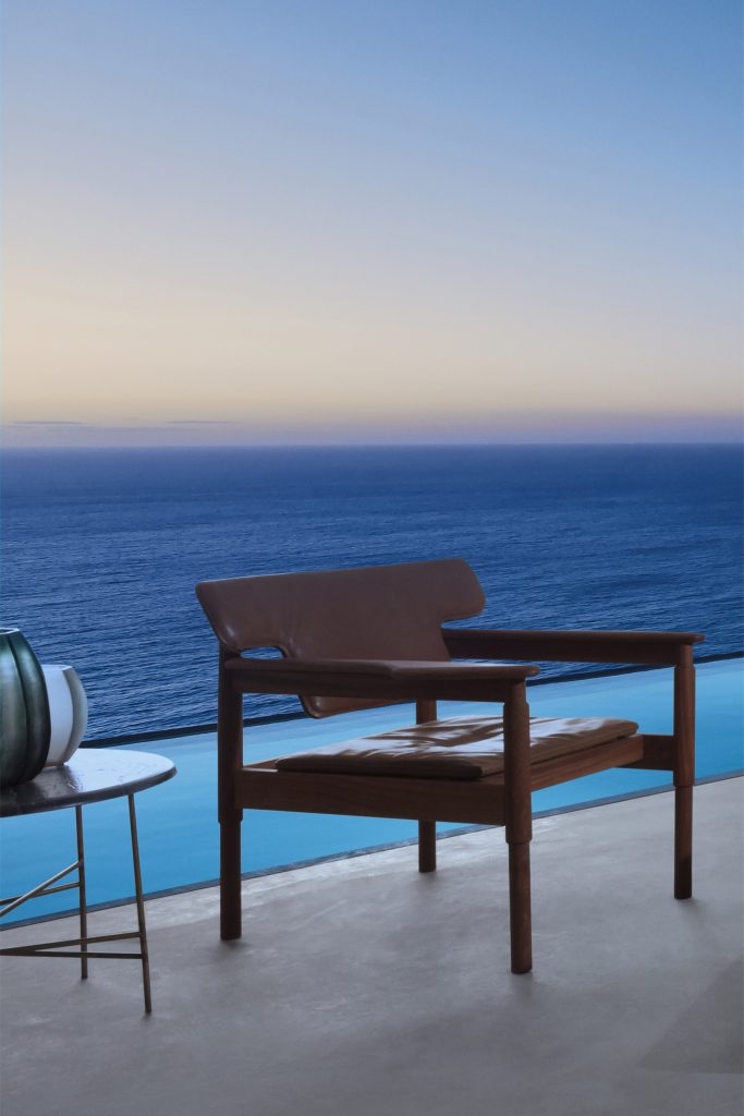 Vieste Armchair: Wooden armchair with a gray cushioned seat with four legs on a terrace.