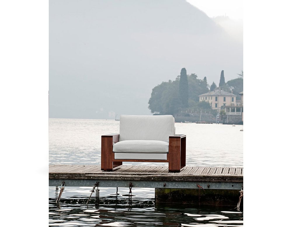 The Bellagio Outdoor Armchair set on a serene dock featuring a solid wooden frame plush cushions and a misty lakefront backdrop