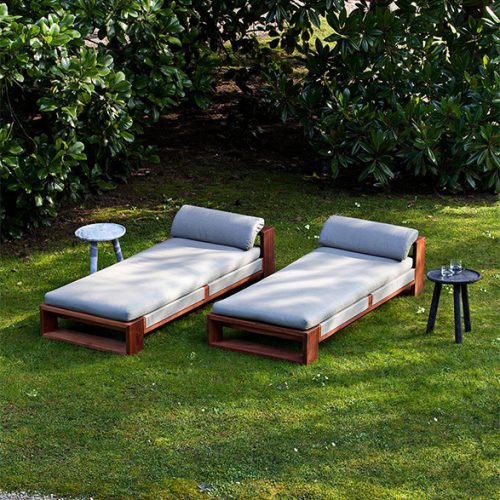 A serene outdoor setting featuring the Bellagio Outdoor Chaise Lounge with plush cushions wooden frames and side tables nestled in lush greenery
