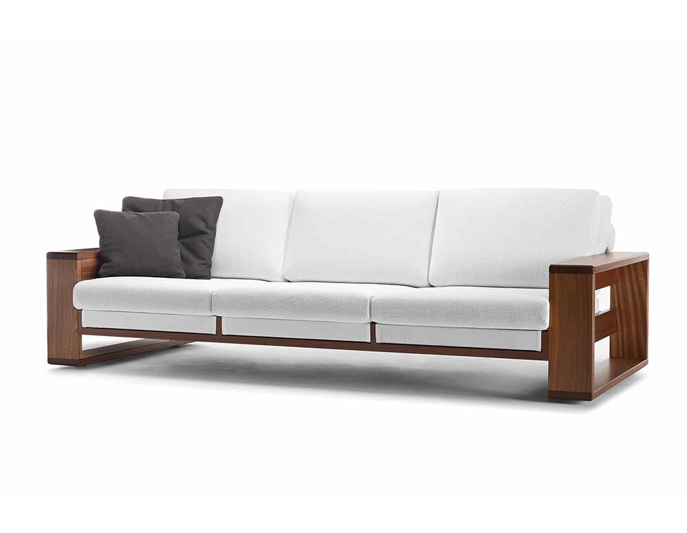 A Bellagio Outdoor Sofa with a wooden frame and white cushions is shown against a white background, with two dark pillows on one side
