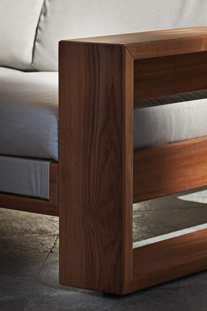Closeup of Bellagio Sofa cushioned in white fabric, strocture and two legs in brown wood.