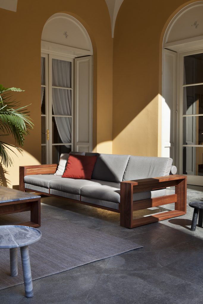 Bellagio Sofa cushioned in white fabric, strocture and two legs in brown wood in a living room.