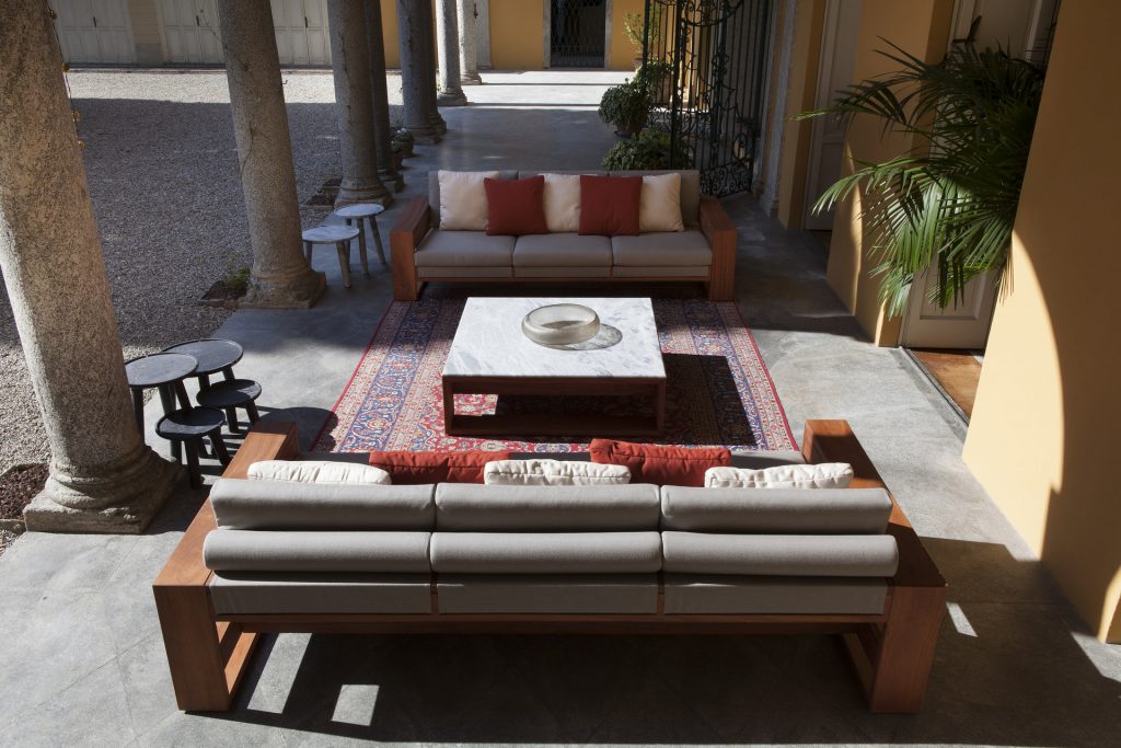 Bellagio Sofa cushioned in white fabric, strocture and two legs in brown wood in a living room.
