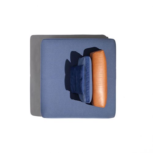 A top-down view of the Caprera Island sofa shows a square, light-colored frame with a dark blue cushion and an orange cylindrical cushion resting against it, all set against a white background