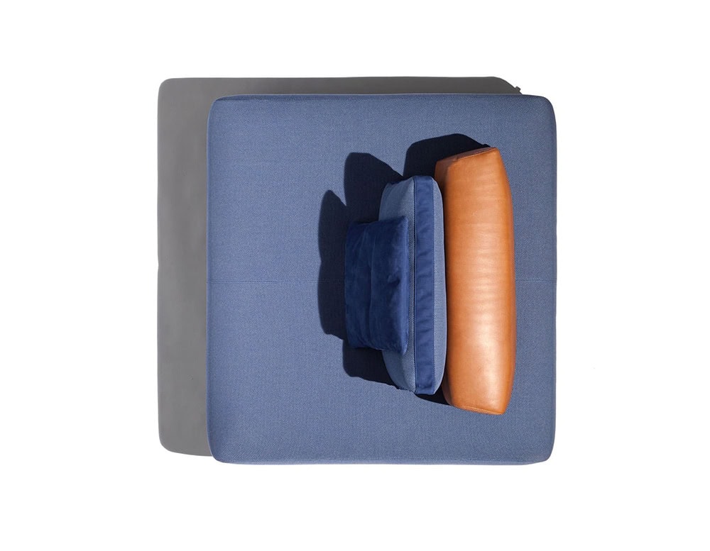 A top-down view of the Caprera Island sofa shows a square, light-colored frame with a dark blue cushion and an orange cylindrical cushion resting against it