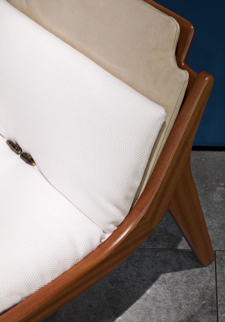 Brown Lerici Armchair with a curved backrest and thin legs with white cushions on a gray background.