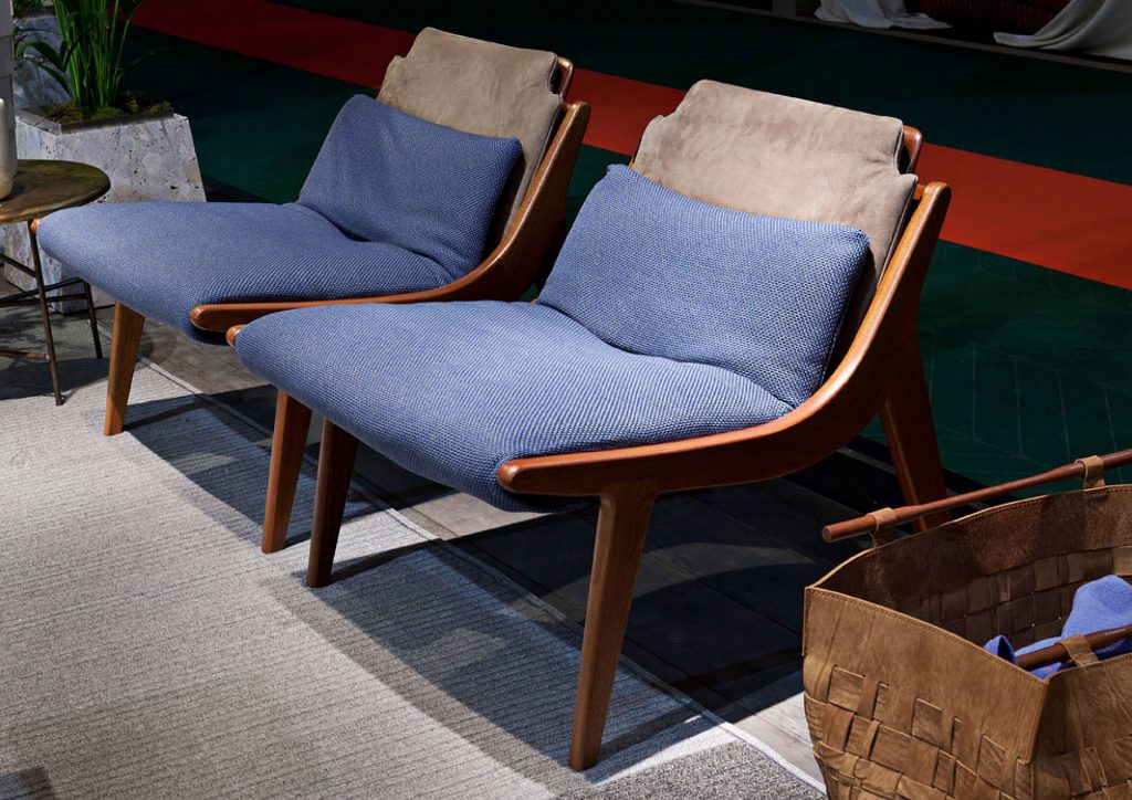 Two brown Lerici Armchairs with a curved backrest and thin legs with blue cushions in a living room.