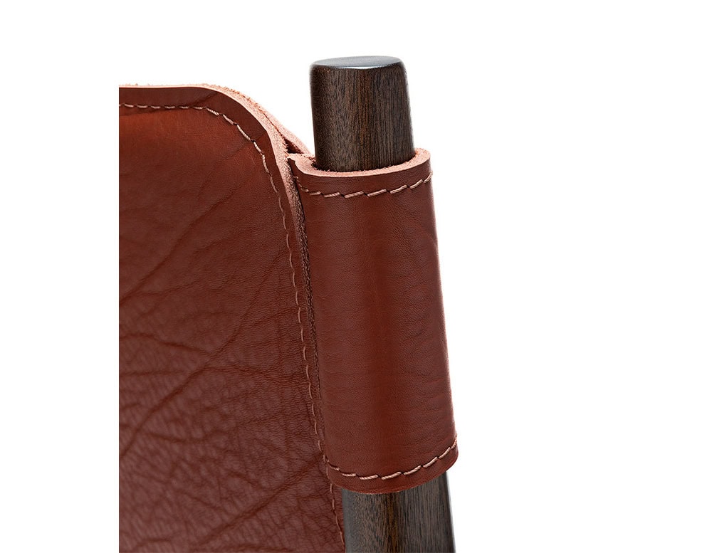 Closeup of Levante Chair. Structure in brown wood, seat and backrest in brown leather on a white background.