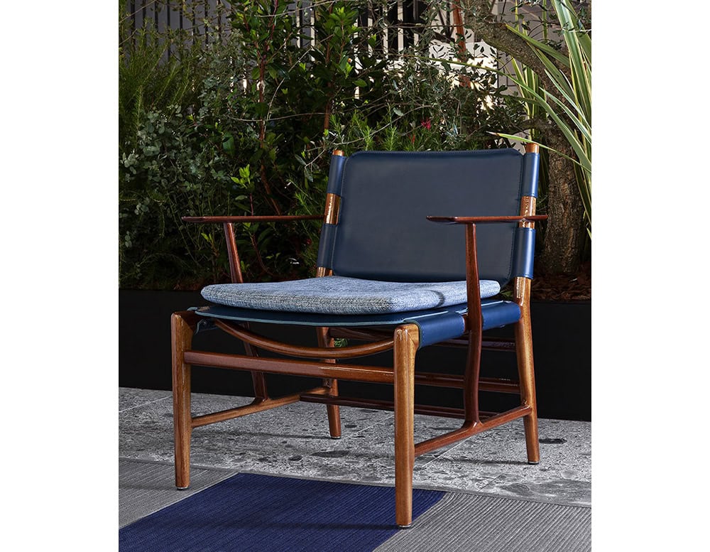 Levante Chair. Structure in brown wood, seat and backrest in blue leather with blue cushions on a terrace.
