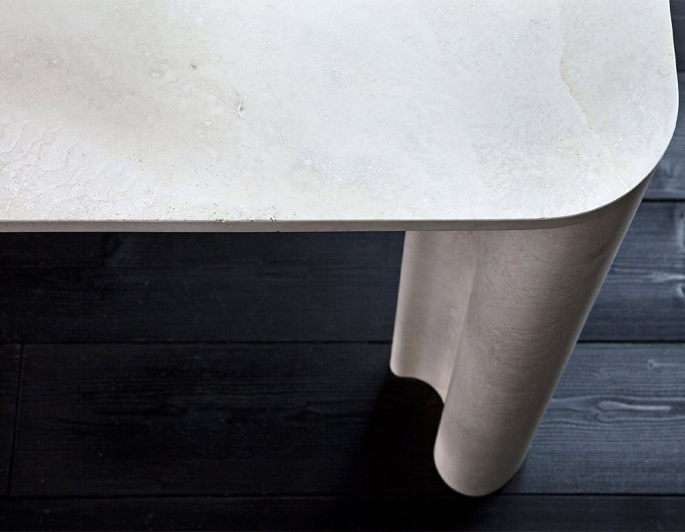 A close-up of a Michaelangelo Dinner Table shows a white table corner with a curved leg and a decorative metal element on a dark surface