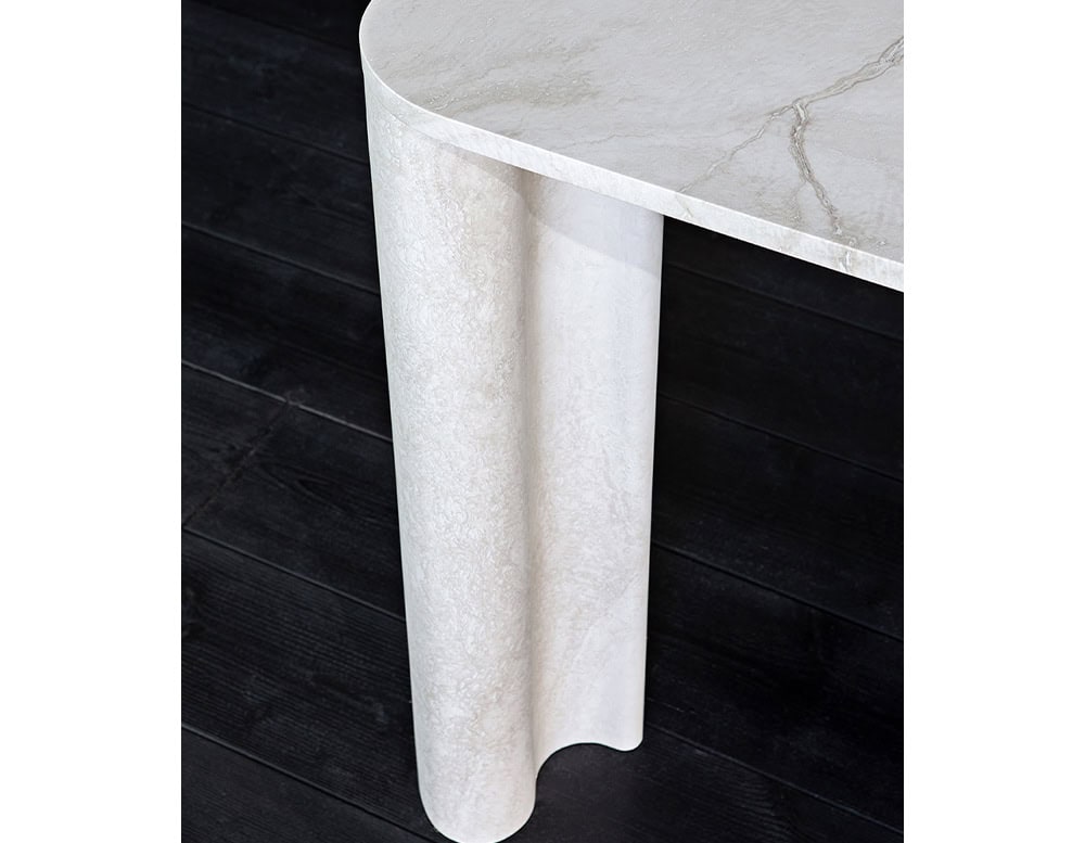 A close-up of a white marble table leg with a fluted design is shown against a dark background