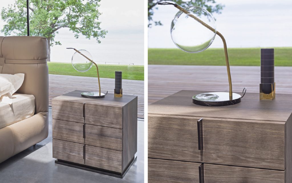 Closeup of a brown wood Ari Night Table with handles and three drawers in a bedroom.