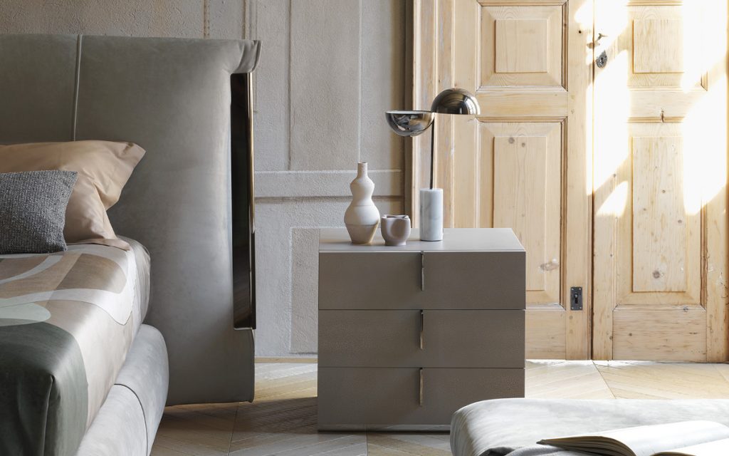 A gray wood Ari Night Table with handles and three drawers in a bedroom.