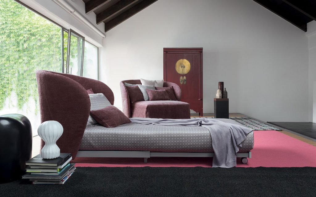 Celine Armchair Sleeper in purple. White, gray and purple pillows and wheels in a bedroom.