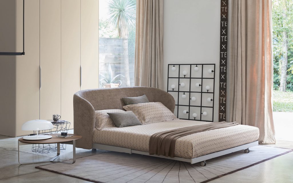 Celine Sofa Sleeper in white and brown bed top, pillows and wheels in a room
