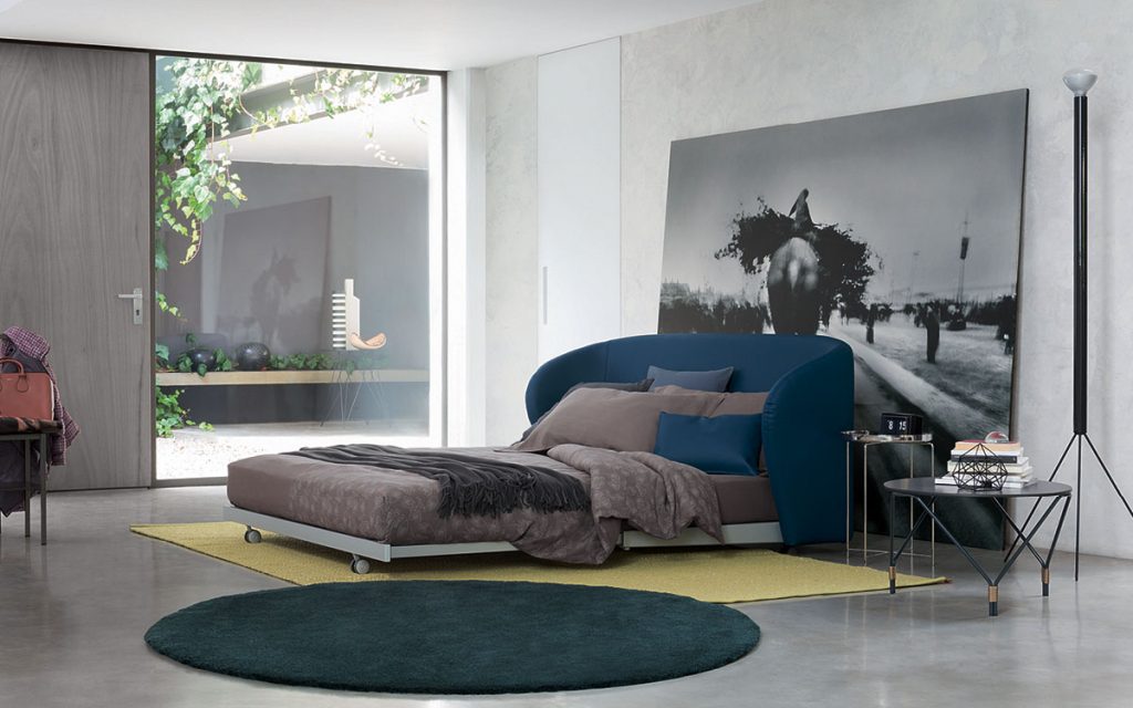 Celine Sofa Sleeper in white and blue brown bed top, pillows and wheels in a bedroom.