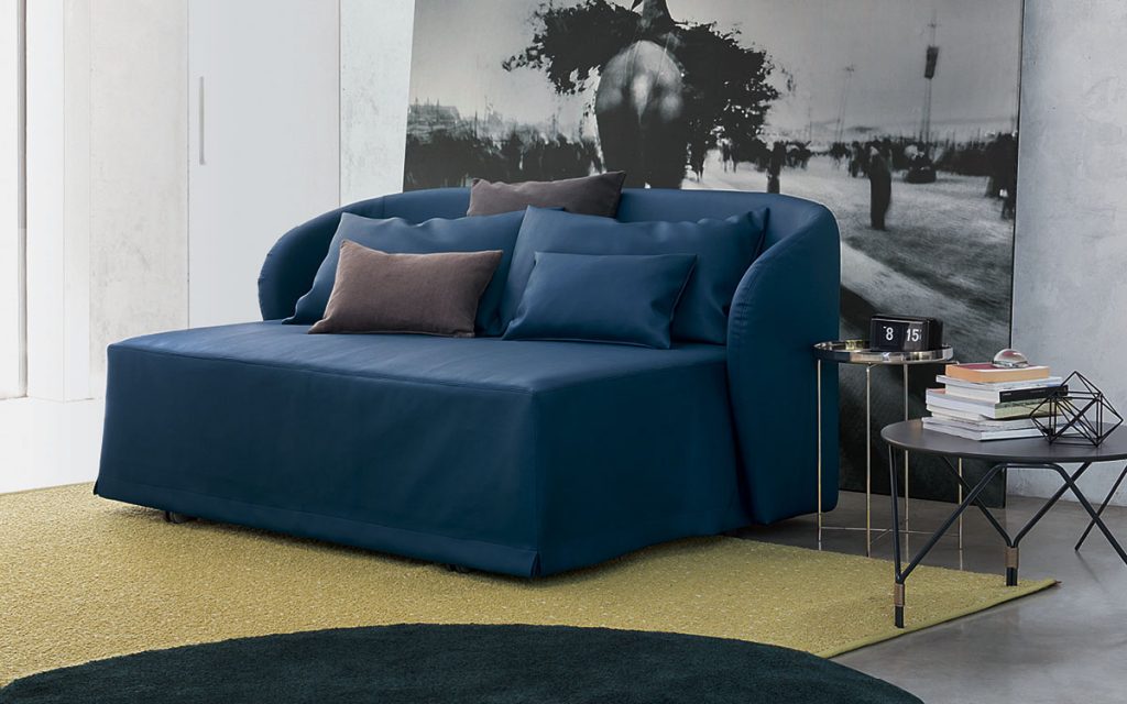 Two Celine Sofa Sleepers in blue, bed top, five pillows and wheels in a bedroom.