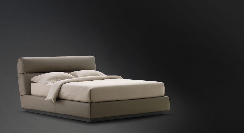 Gentleman Low. Base and high headboard upholstered in gray fabric with bedding on a black background.