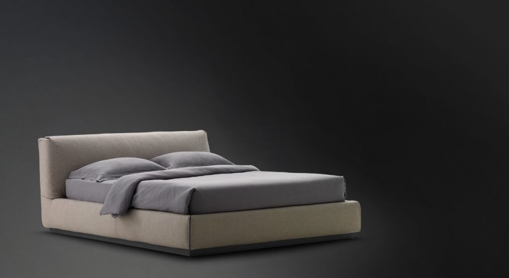 Gentleman Low. Base and headboard upholstered in gray fabric with bedding on a black background.