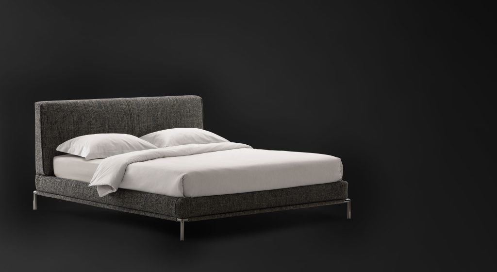 Icon bed. Base and heardboard padded in gray fabric with black steel legs on a black background.