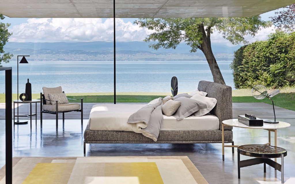 Icon bed. Base and heardboard padded in gray fabric with black steel legs in a bedroom.