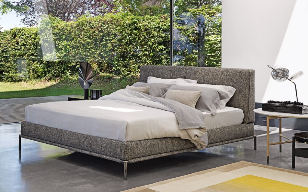 Icon bed. Base and heardboard padded in gray fabric with black steel legs in a bedroom.