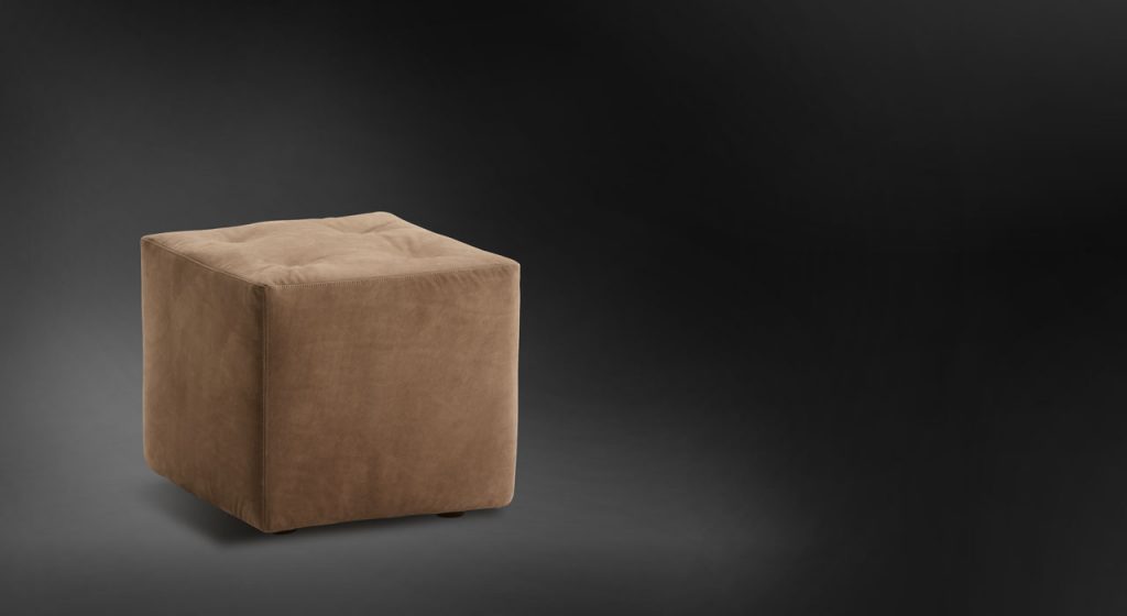 Iko Pouf with cubic shape upholsted in brown fabric on a black background.