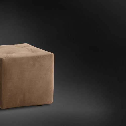 Iko Pouf with cubic shape upholsted in brown fabric on a black background.